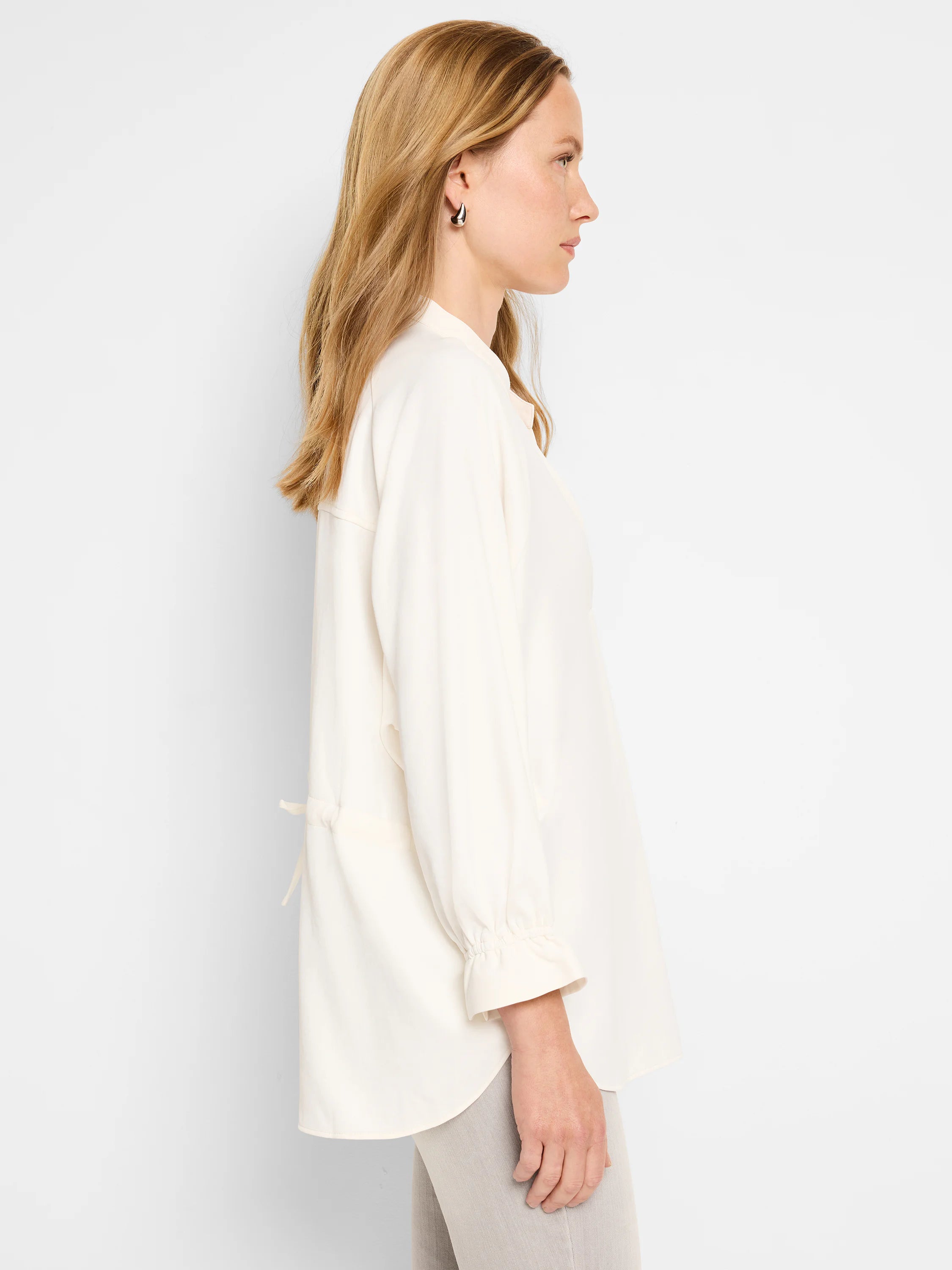 Off-white, loose-fitting blouse with long sleeves and a slightly curved hem. Back features a drawstring detail.