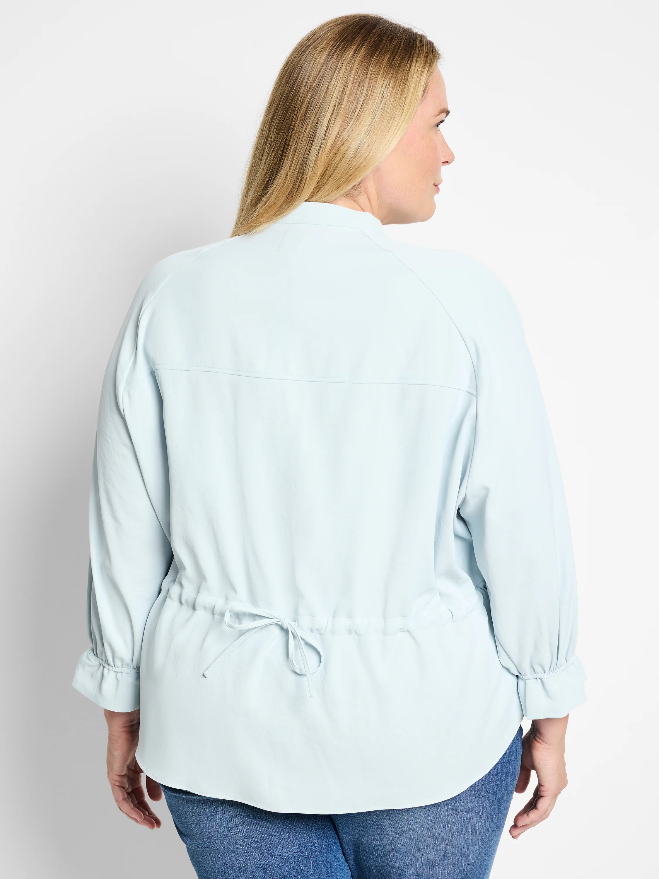 Light blue, long-sleeve blouse with cinched waist and slight puff sleeves. Back view.