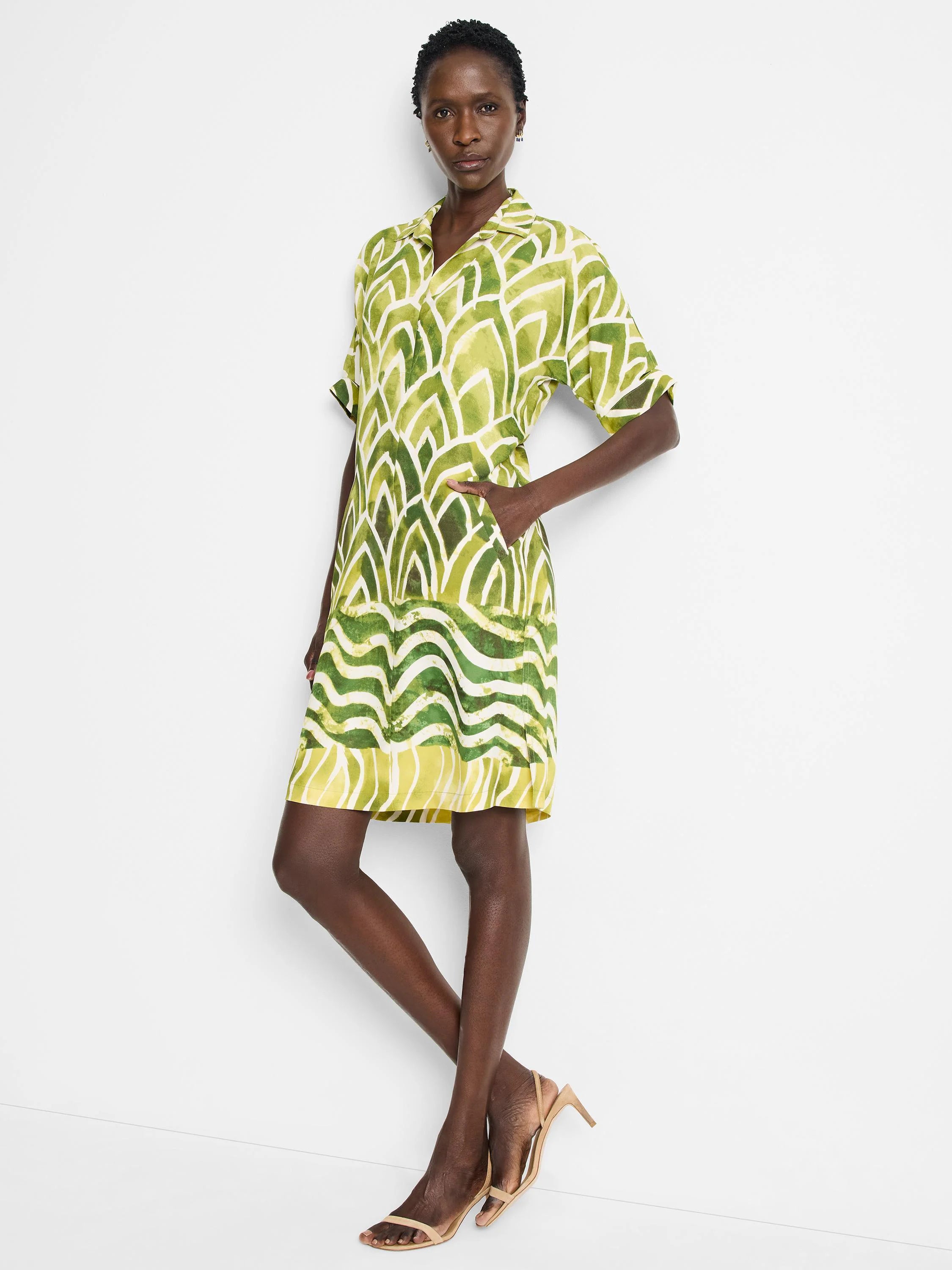Short, collared shirt dress in green and yellow abstract print. Features short sleeves and pockets.