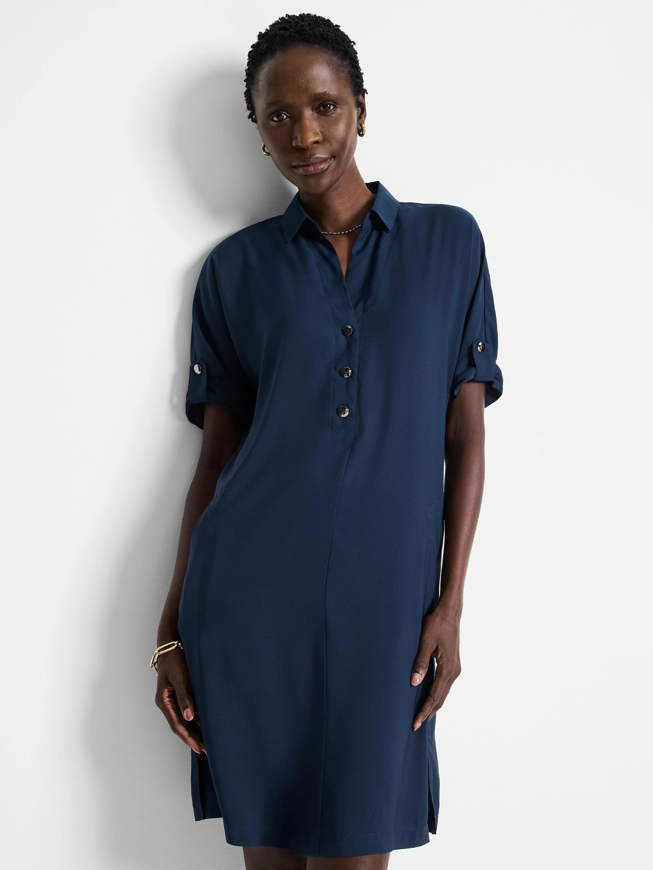 Dark blue button-front collared shirt dress with rolled short sleeves and tab details. Hits at mid-thigh.