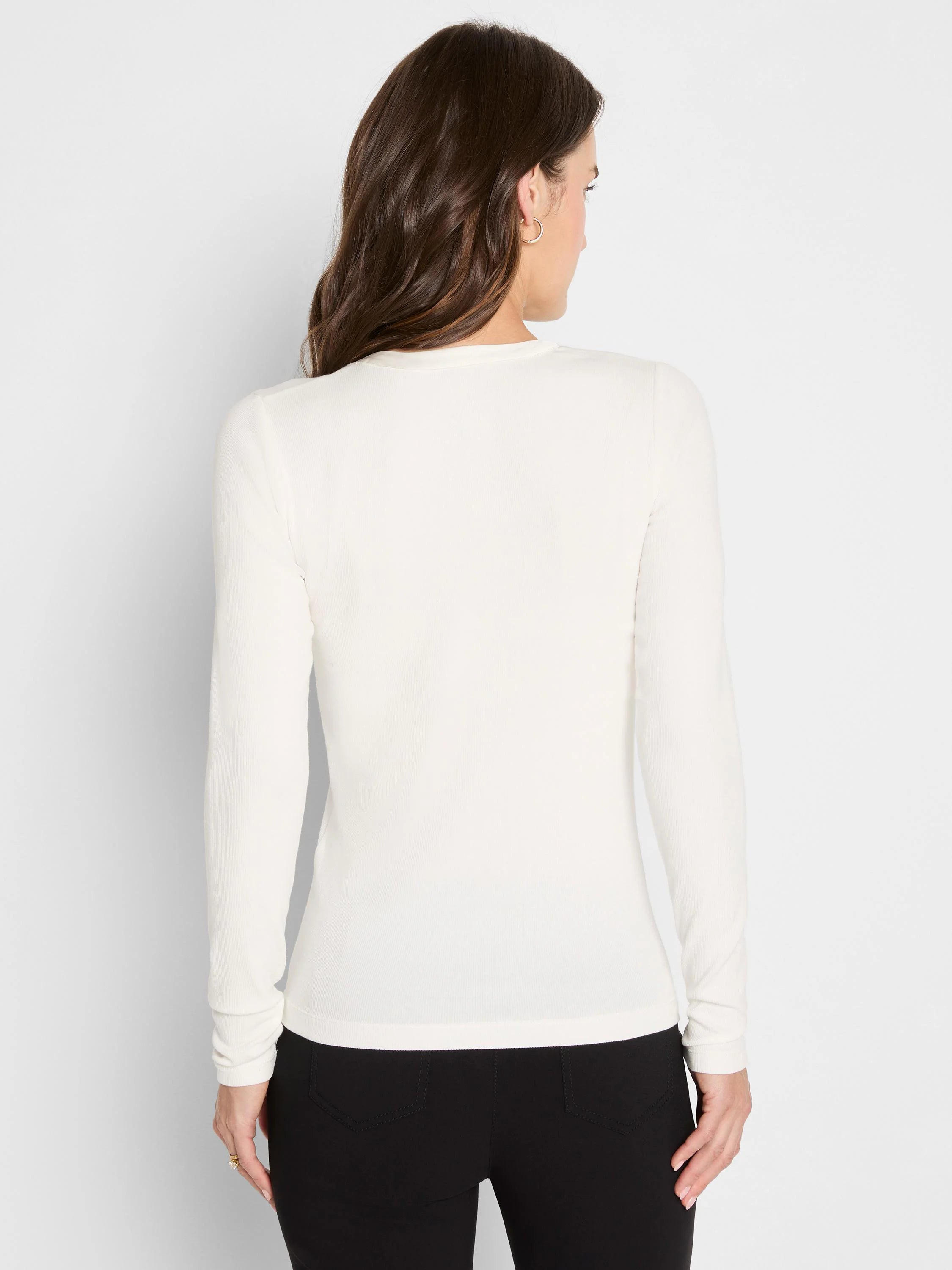 Back view of a woman wearing a cream, long-sleeve, fitted ribbed knit top.