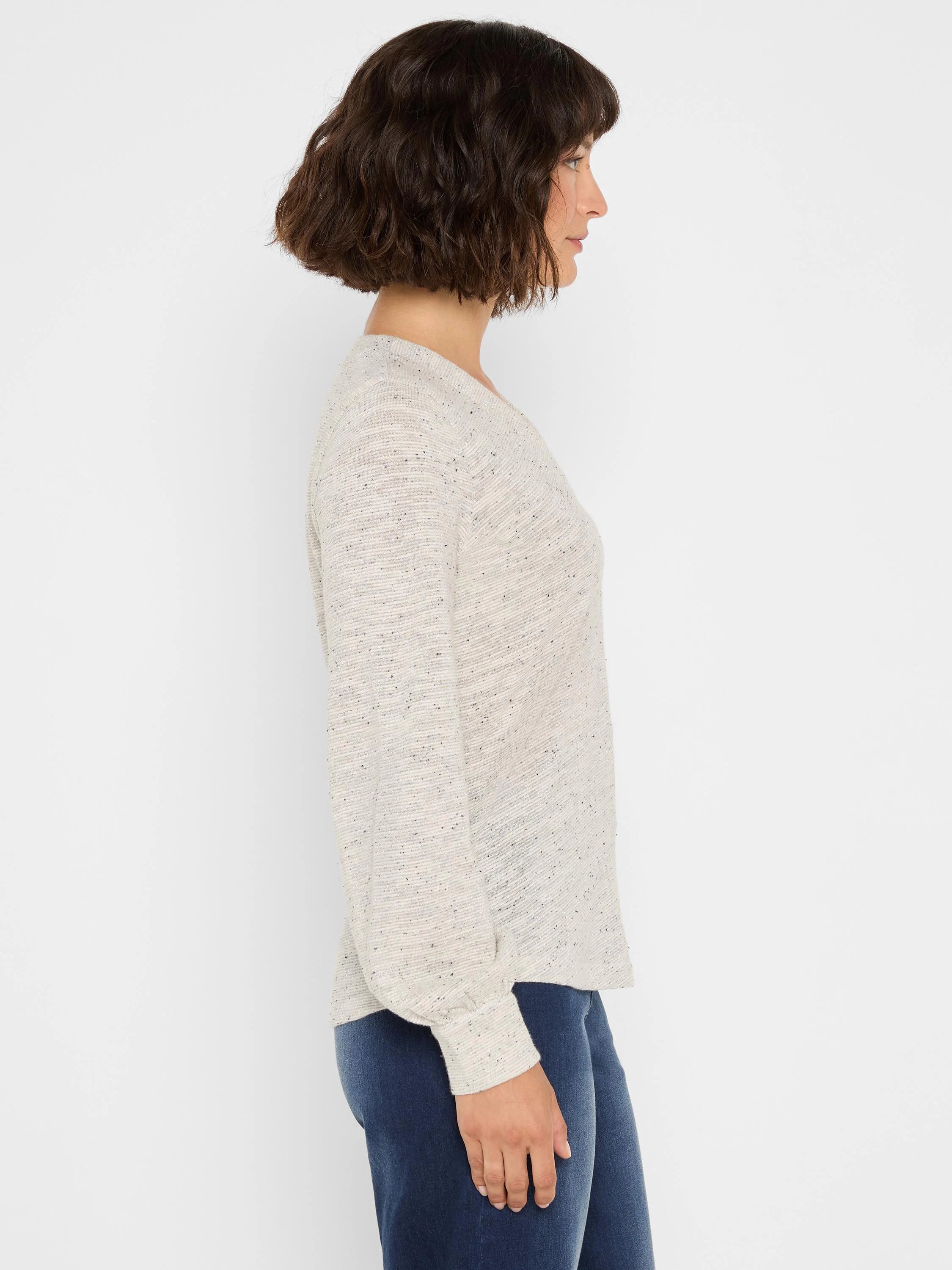 Light cream long-sleeve knit top with dark speckled flecks and subtle sparkle. Relaxed fit. Model in profile.