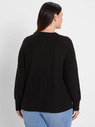 Black waffle-knit cardigan, seen from the back, with long sleeves, ribbed cuffs, and hem.