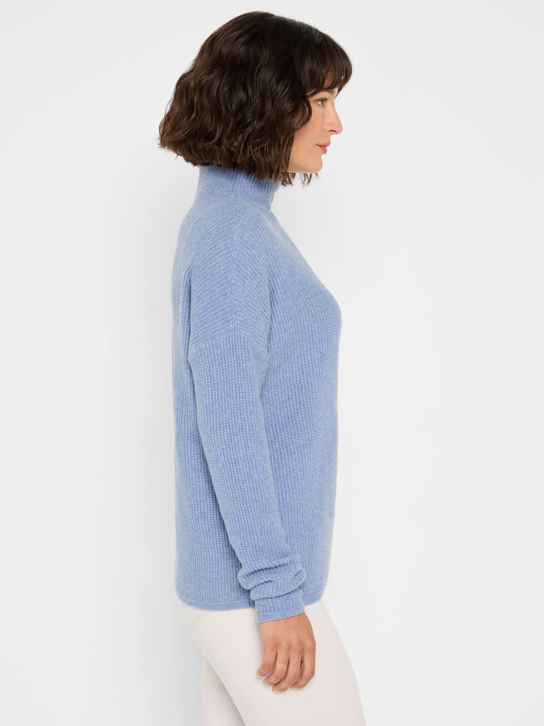 Periwinkle blue waffle-knit turtleneck sweater with a relaxed fit and long sleeves, modeled in profile.