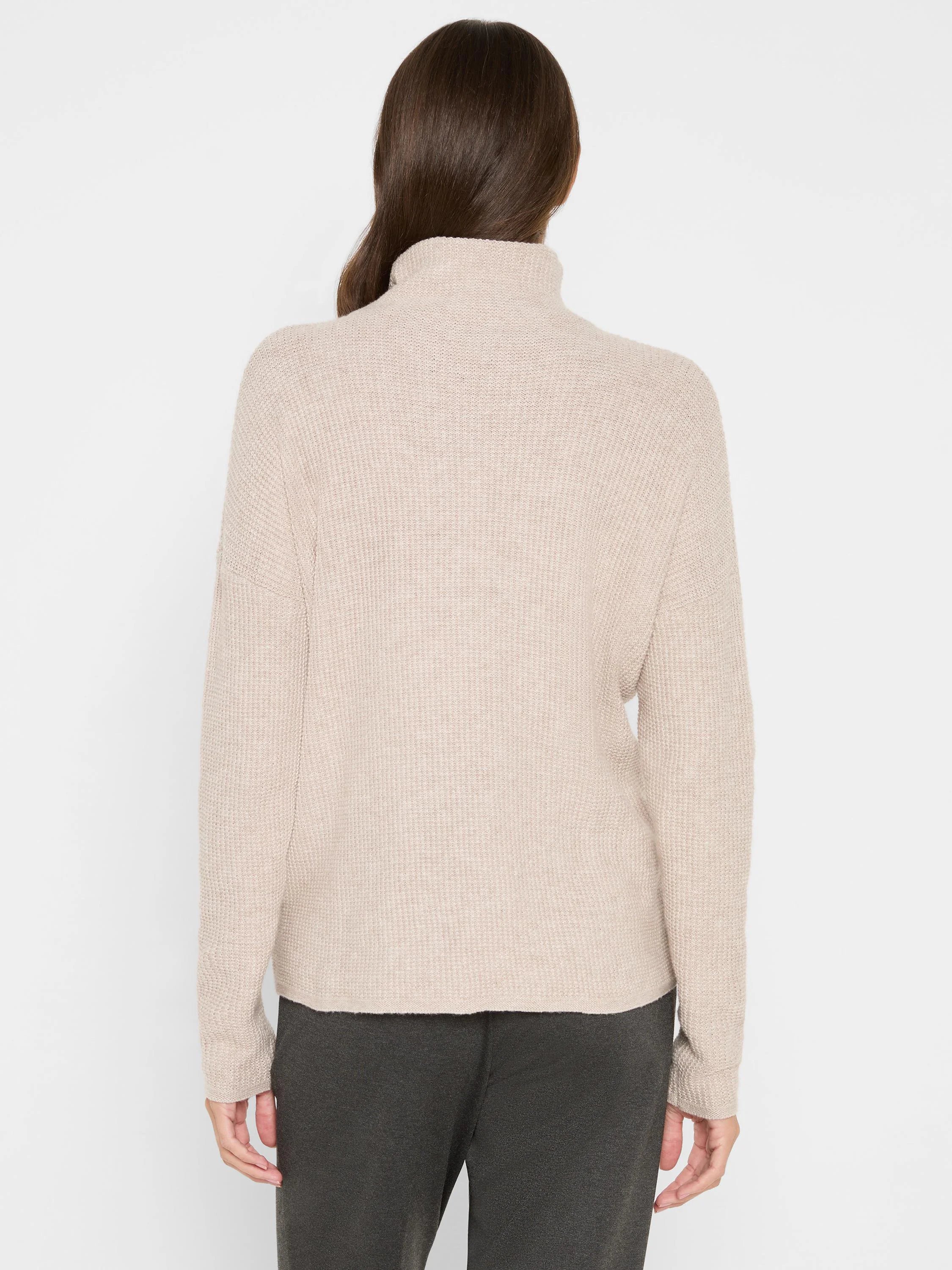 Back view of a light beige waffle knit turtleneck sweater with a relaxed fit, on model.