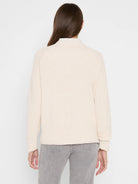 Back view: cream shaker stitch sweater with crew neck, ribbed cuffs & hem. Layered over a striped shirt.