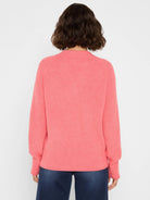 Coral pink shaker stitch sweater, back view, on a model. Features ribbed knit texture, long sleeves, ribbed cuffs, and hem.