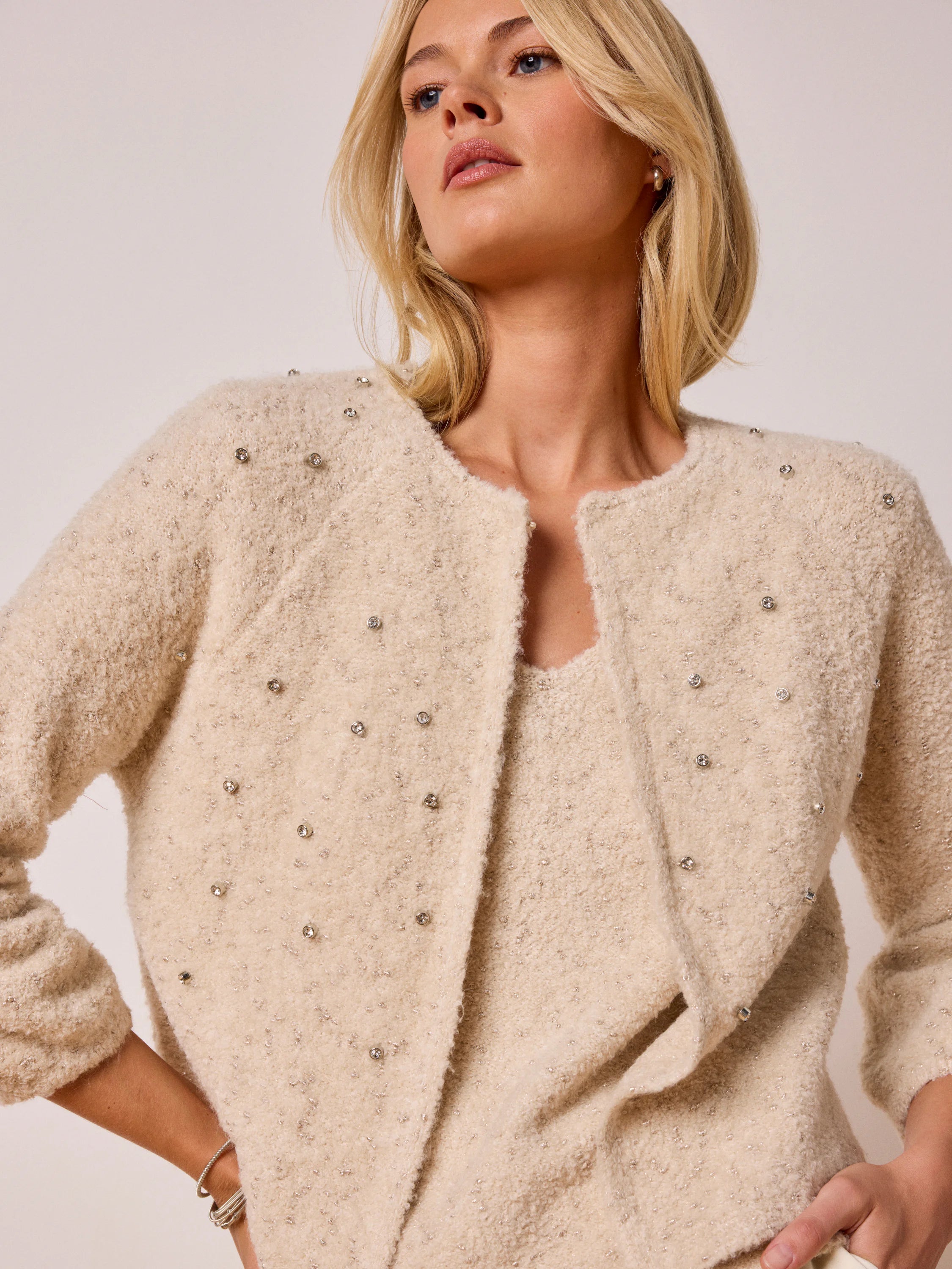 Light beige textured knit tank with subtle metallic flecks, worn under a matching open cardigan embellished with silver...