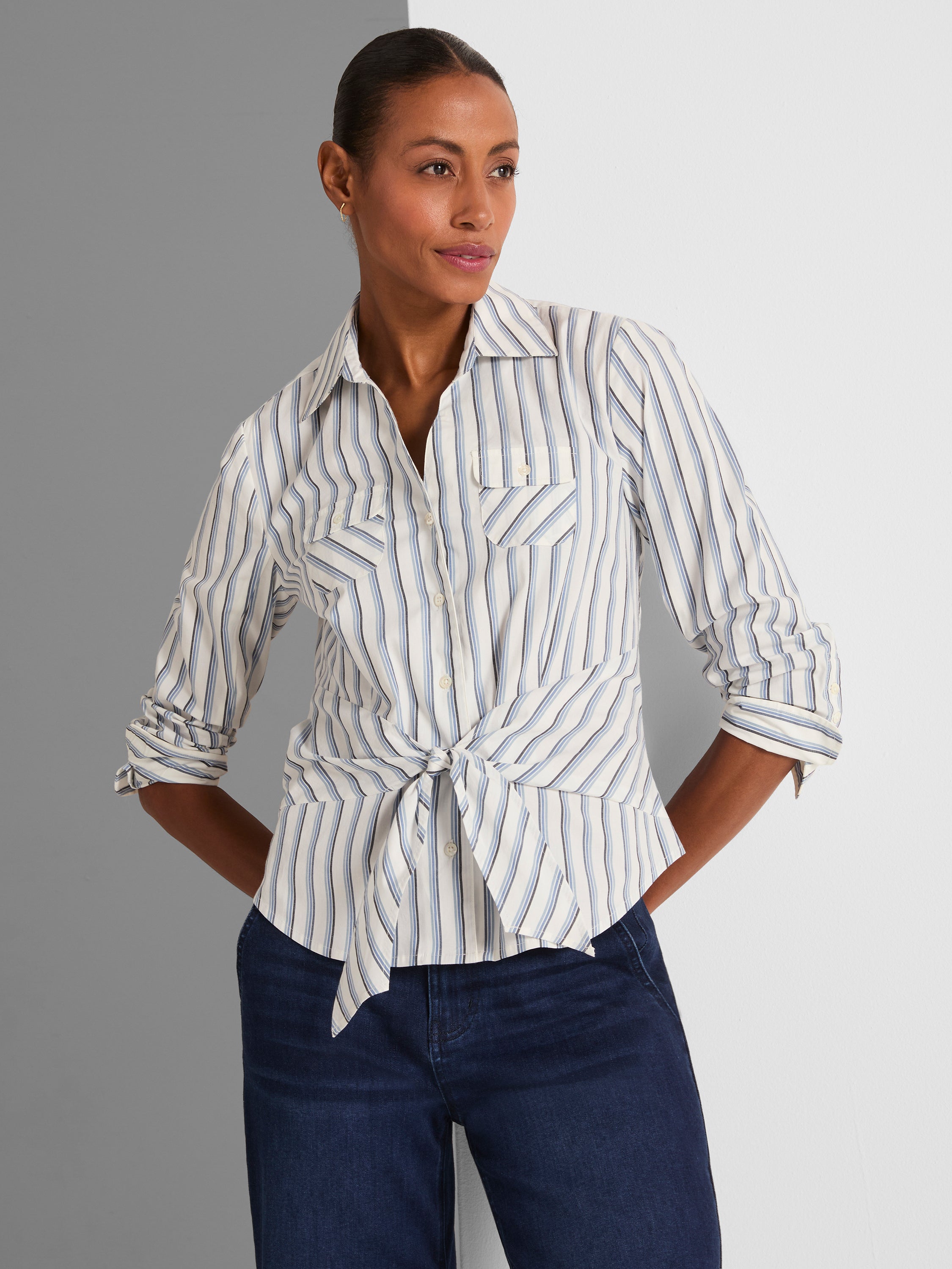 A white and blue striped button-down shirt features front flap pockets and a casual tied knot at the waist hem.