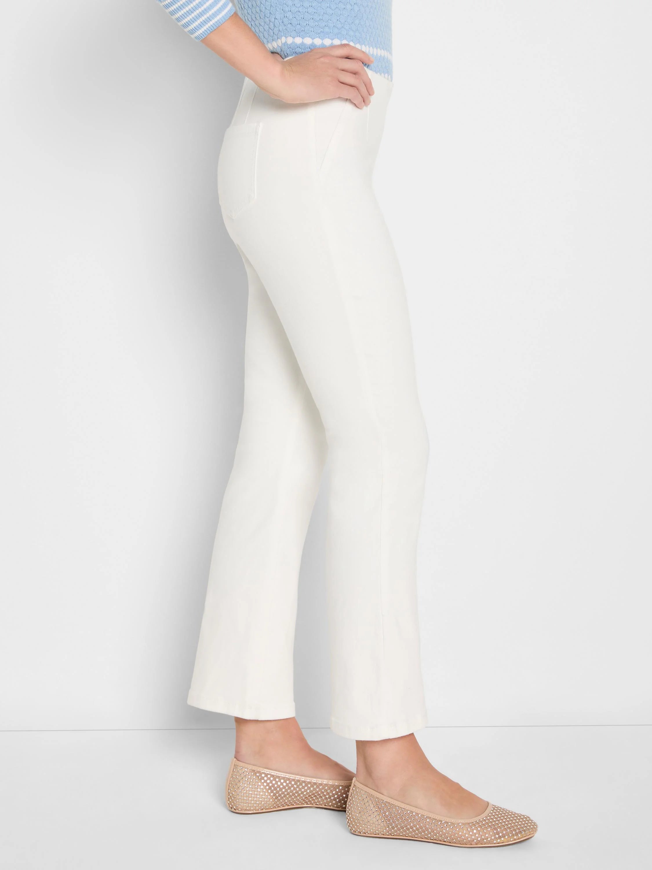 White bootcut jeans on a model, side view. High waist, slim through the thigh, with a gentle flare at the hem.
