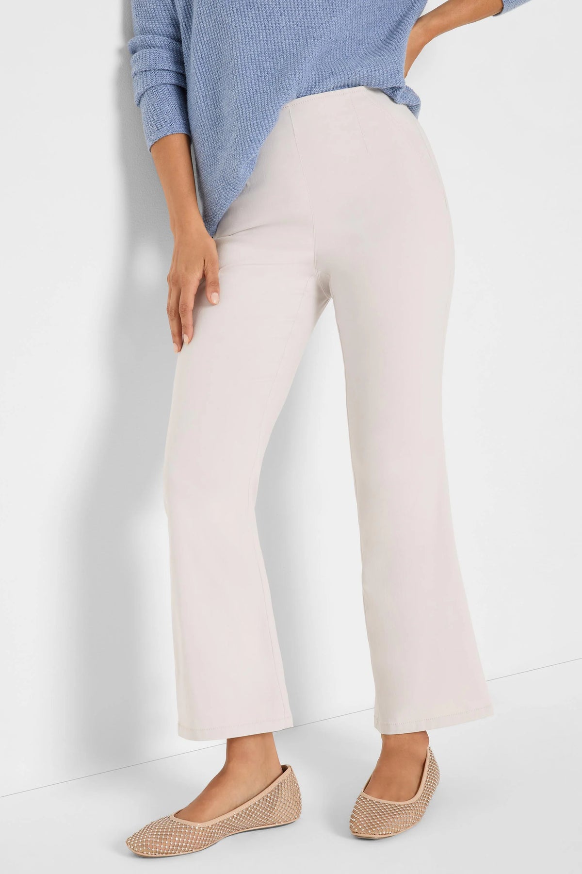 Light beige high-waisted bootcut pants with smooth fabric, worn by a model.