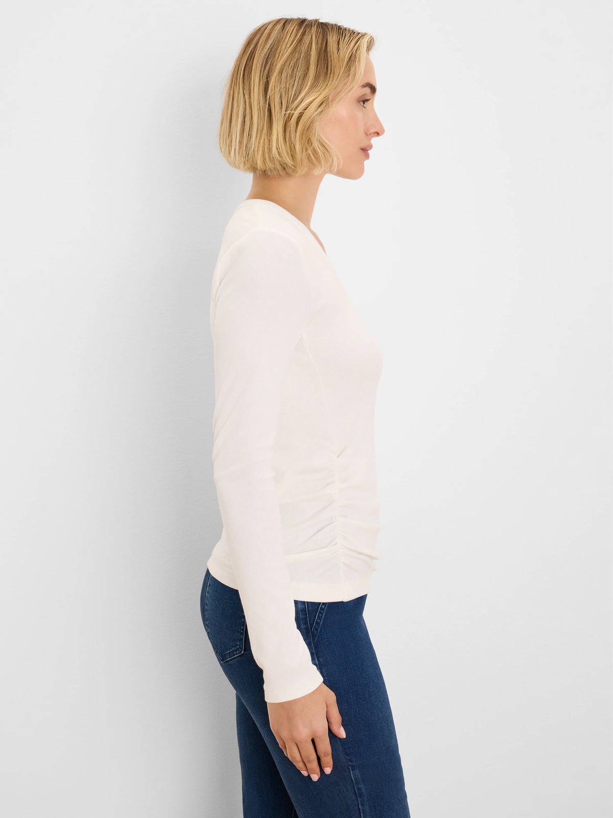Off-white rib knit long-sleeve tee with side ruching, shown on a model in profile.