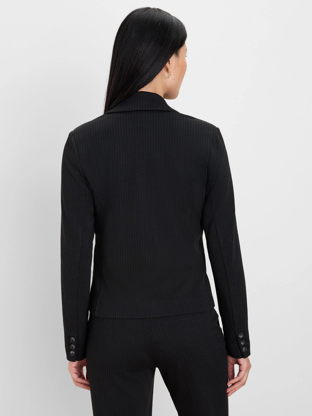 Black blazer with thin light pinstripes, three dark buttons on each sleeve cuff. Model's back to camera.