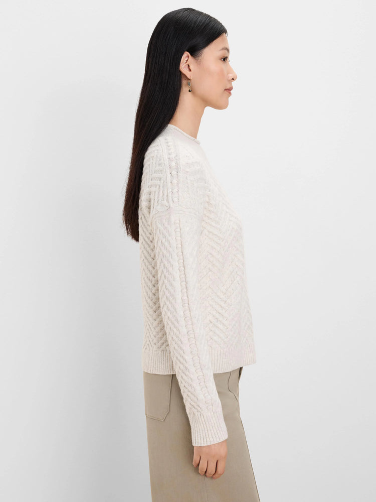 Cream roll neck sweater with cable knit sleeves featuring bobbles, and a chevron pattern on the body.