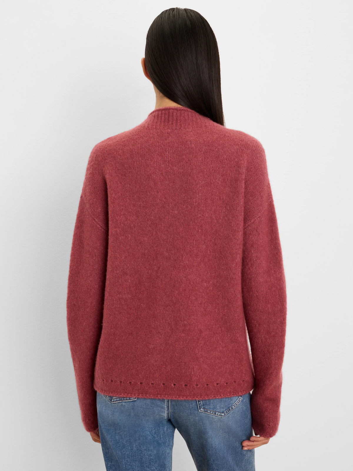 Back view: Dusty rose fuzzy knit mock neck sweater with a perforated hem, worn by a model in blue jeans.