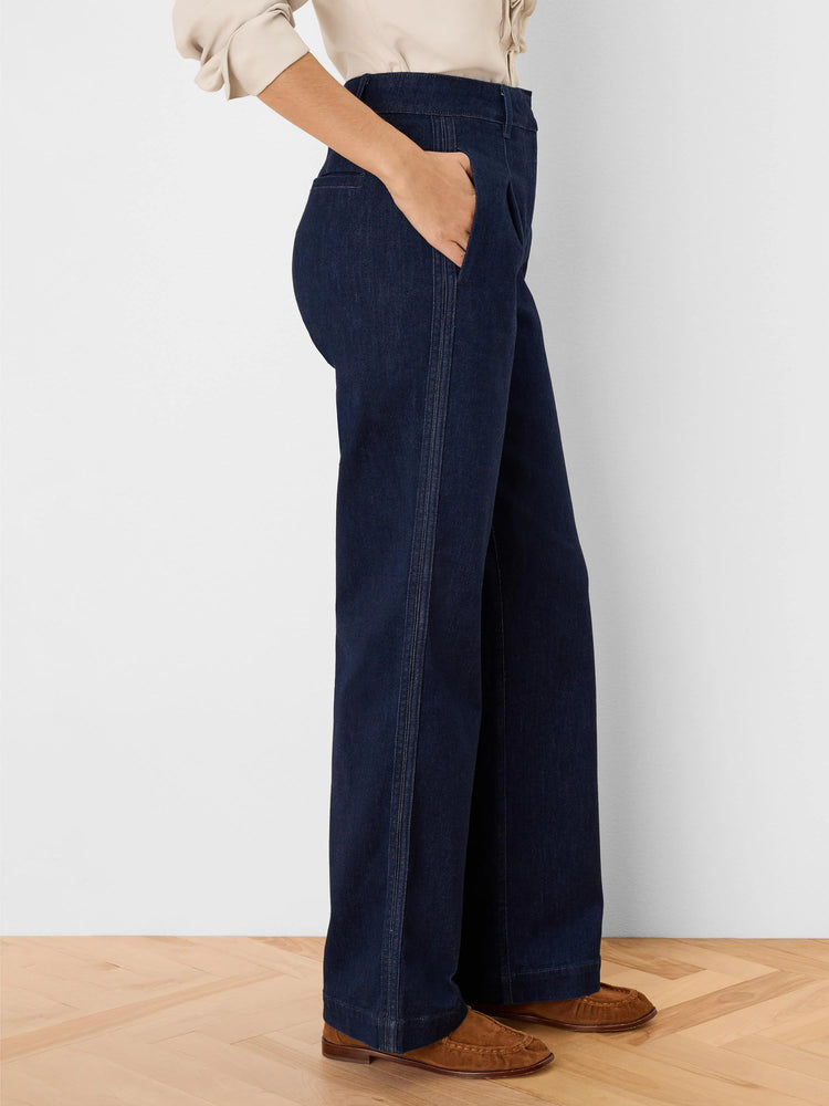 Dark indigo wide-leg denim trousers with vertical double-stitched front seams. A hand rests in a pocket.