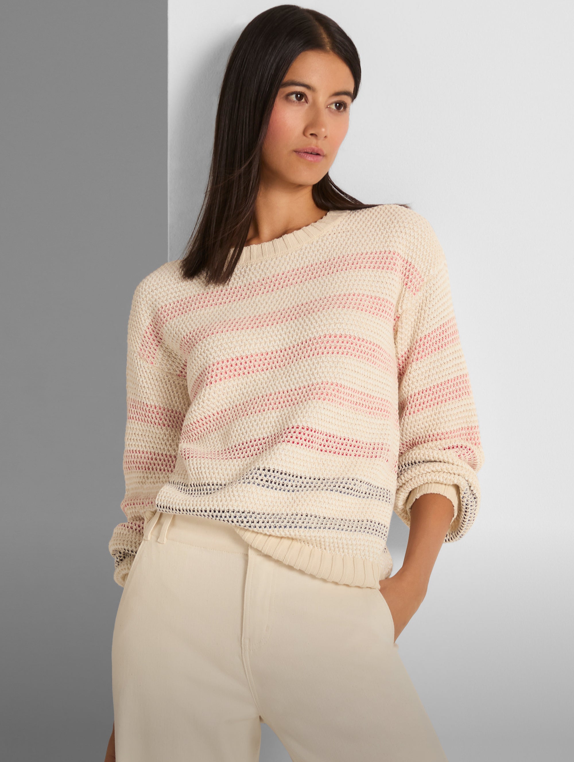 Woman wearing a striped sweater and beige pants against a gray background