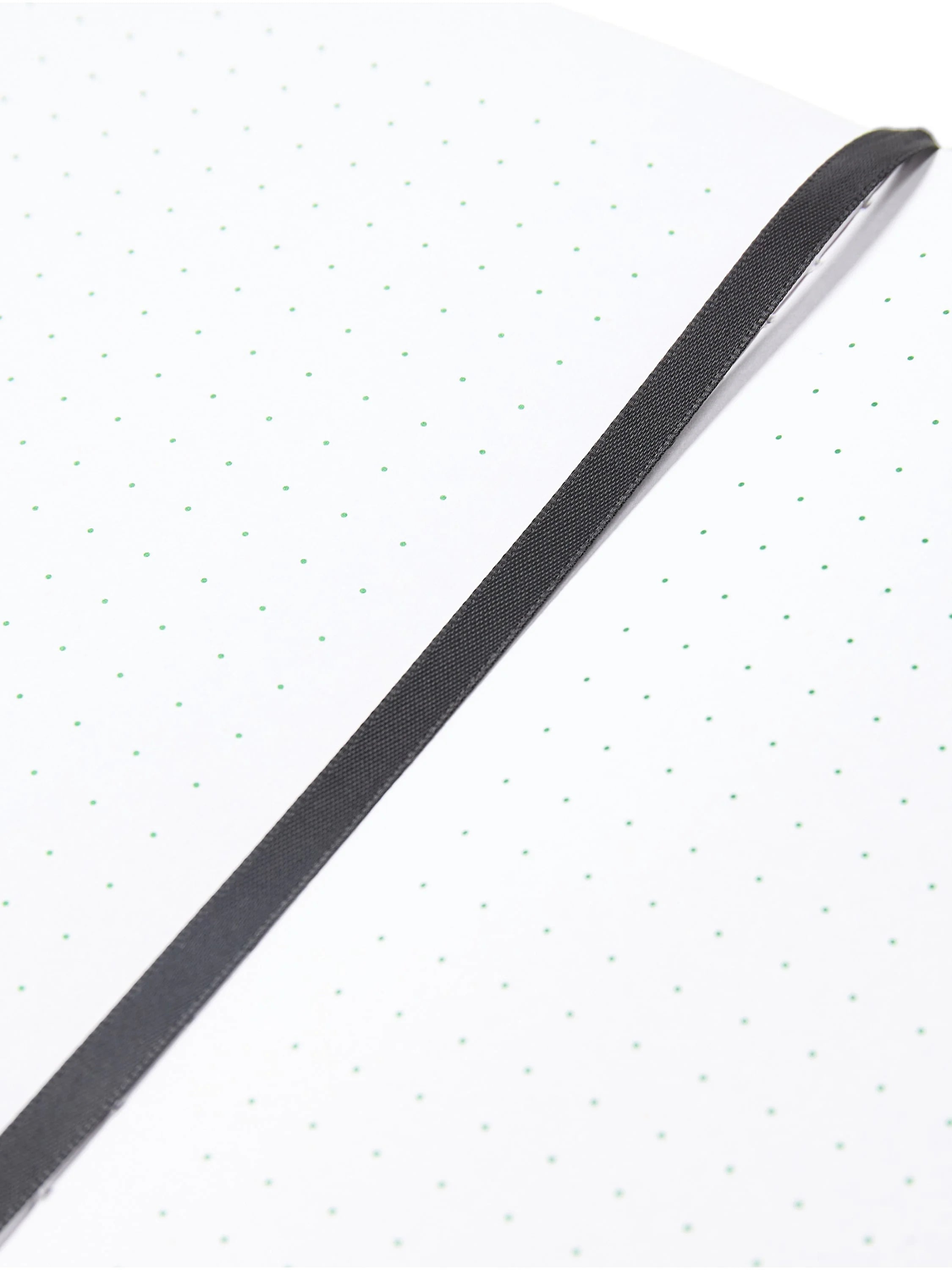 Open notebook page: white with light green dot grid. A dark gray fabric bookmark lays diagonally across.