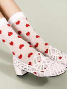 Sheer socks with a red heart pattern are worn inside white leather caged flats featuring a low block heel.
