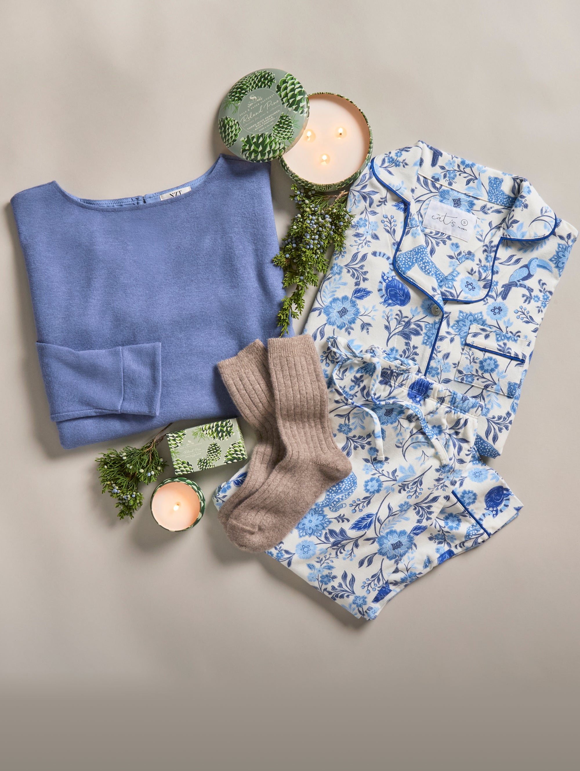 Blue sweater, floral pajama set, and brown socks on a neutral background with candles and greenery.