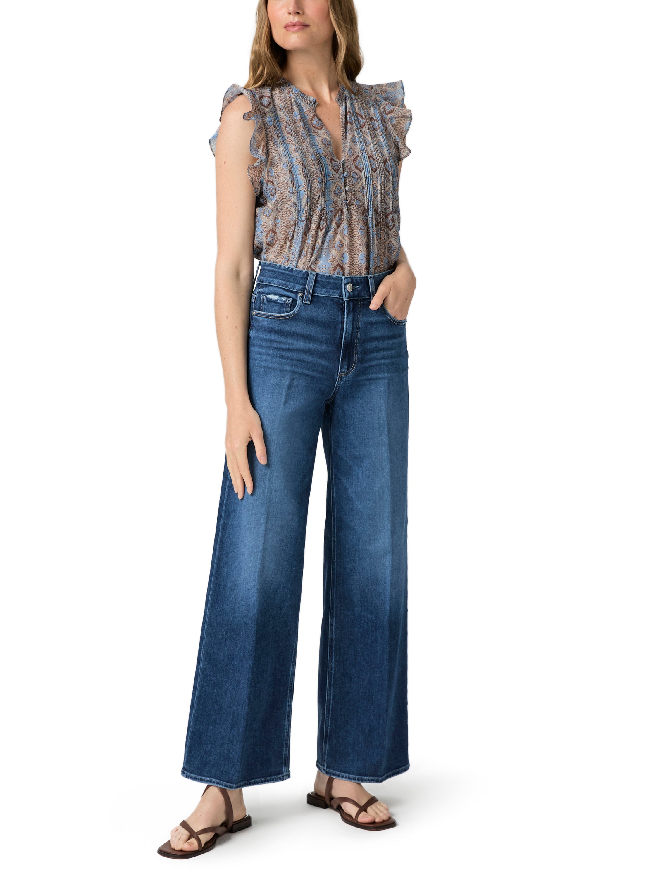 A patterned ruffled V-neck blouse is tucked into high-waisted, dark wash wide-leg denim pants.