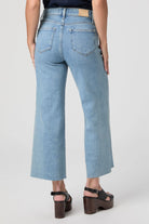 Light blue denim jeans with back pockets, a brown leather waist patch, and a frayed cropped hem.