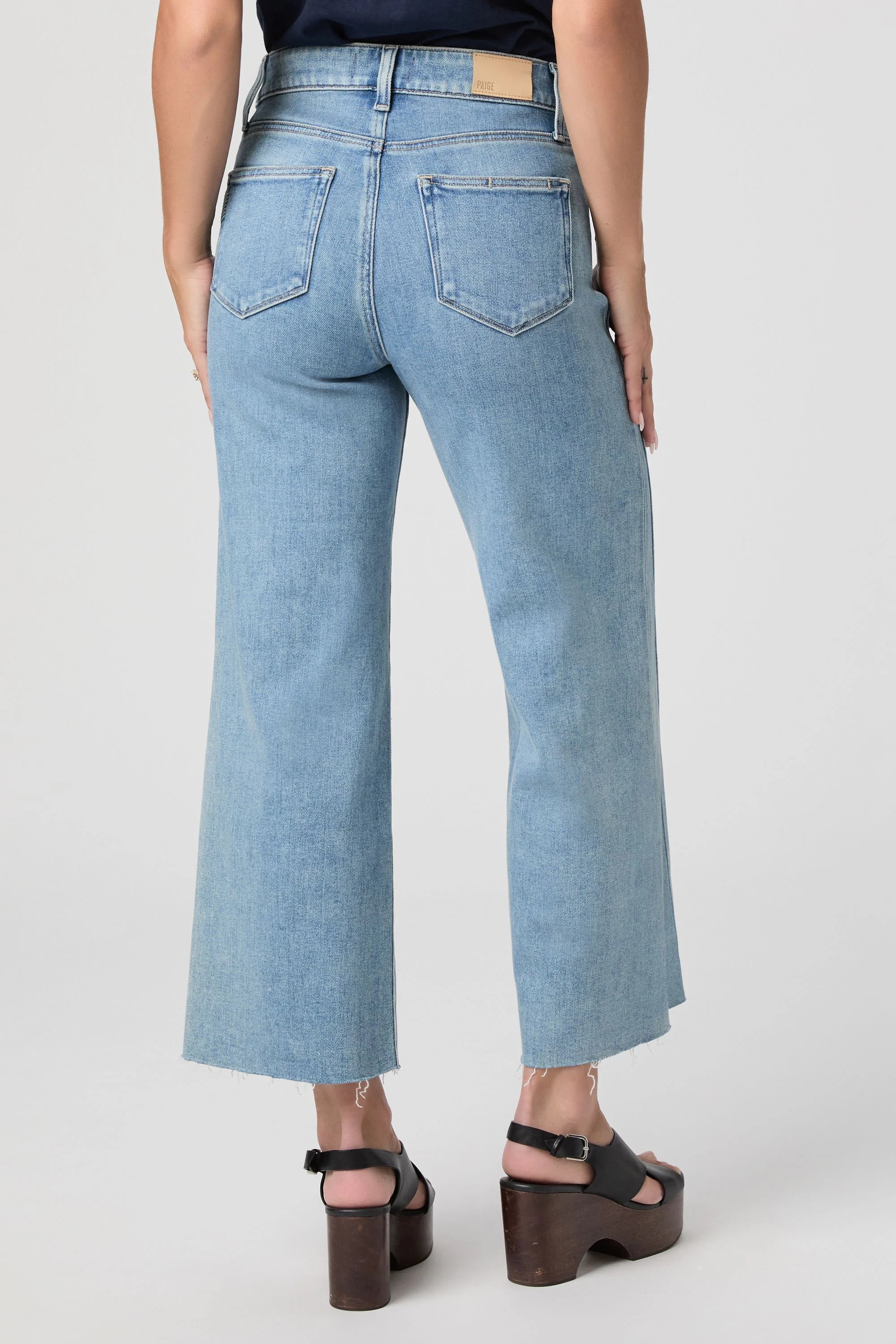 Light blue denim jeans with back pockets, a brown leather waist patch, and a frayed cropped hem.