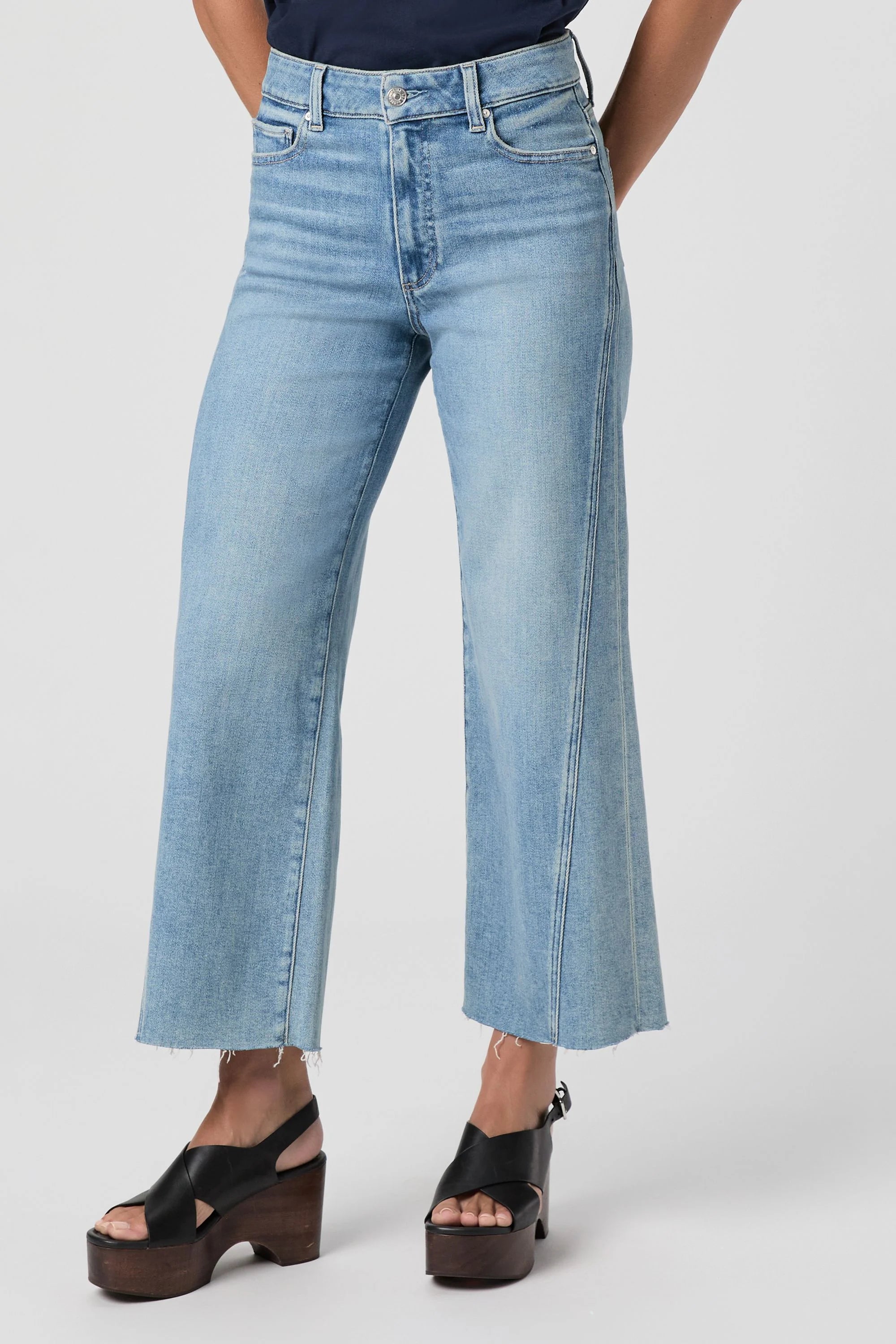 Light wash blue high-waisted wide-leg jeans with a twisted outseam panel and frayed raw hems.