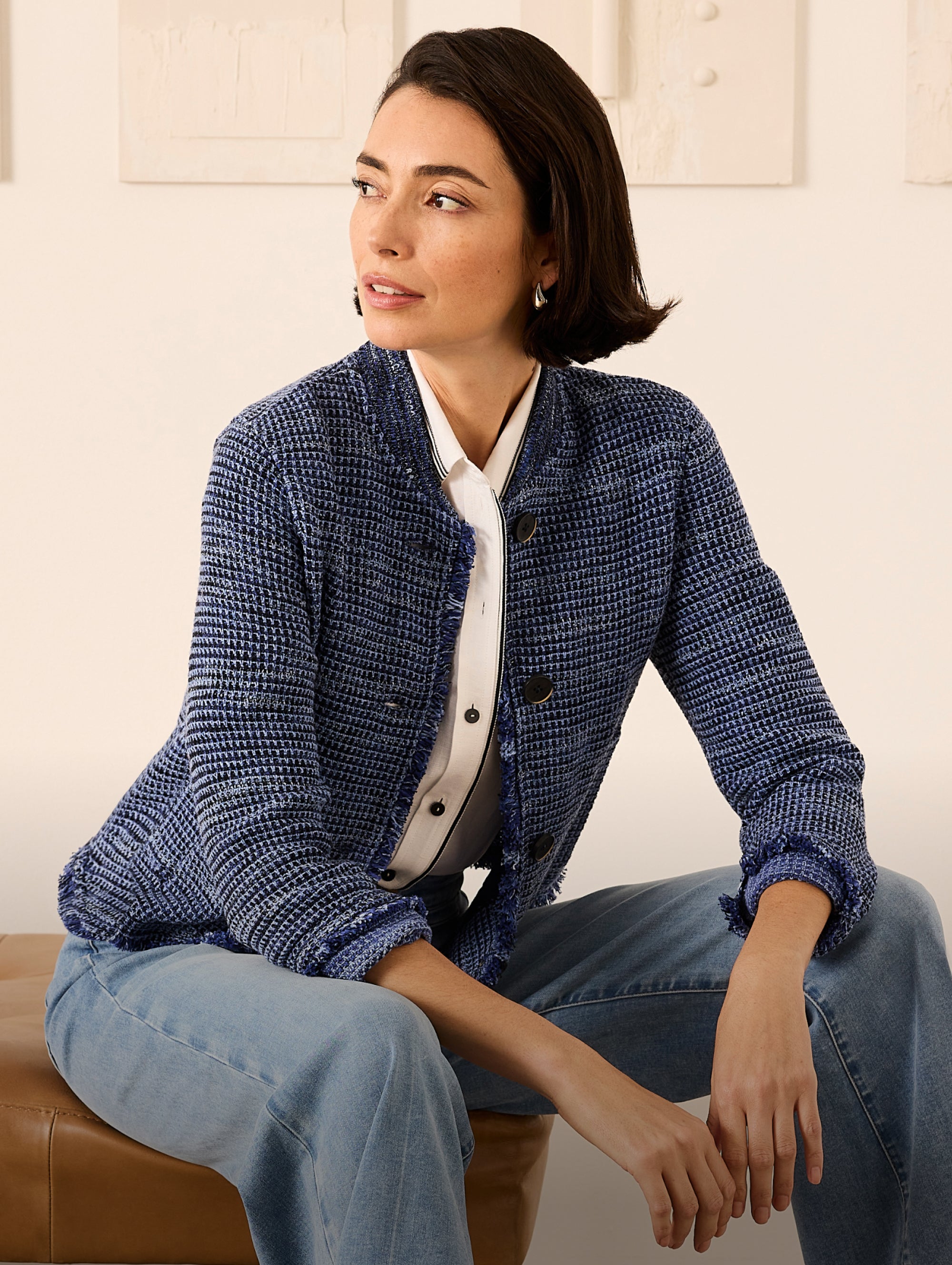 Woman wearing a blue textured jacket sitting on a couch.