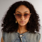 Translucent nude cat-eye sunglasses with rose-brown gradient lenses on a model's face.