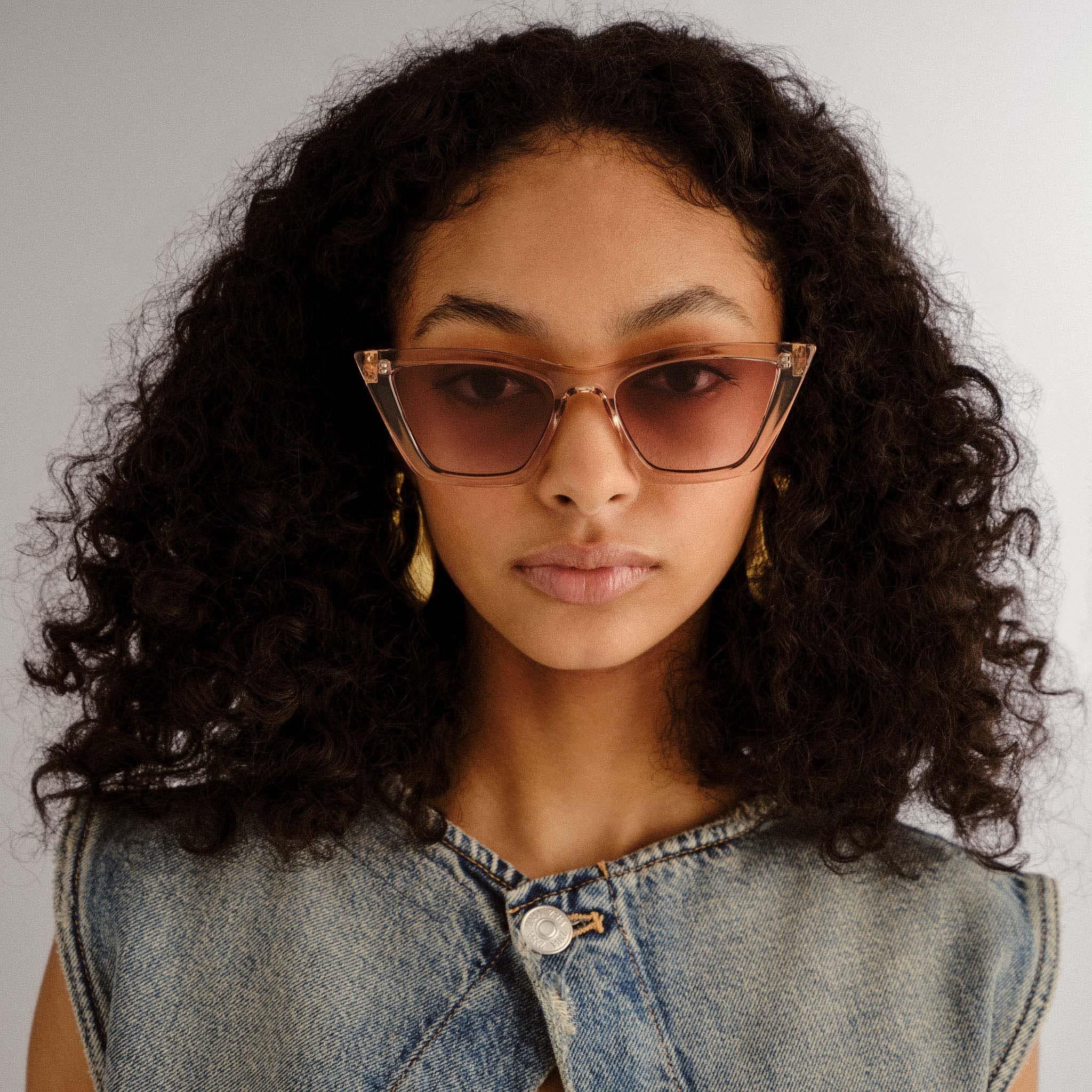 Translucent nude cat-eye sunglasses with rose-brown gradient lenses on a model's face.