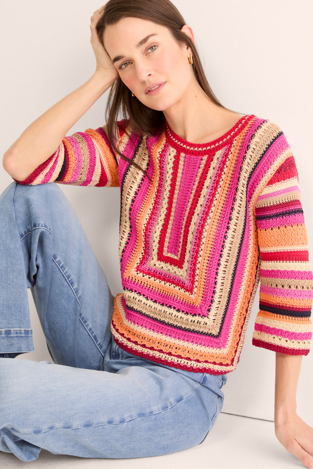 Woman wearing a colorful striped sweater sitting on a white surface.