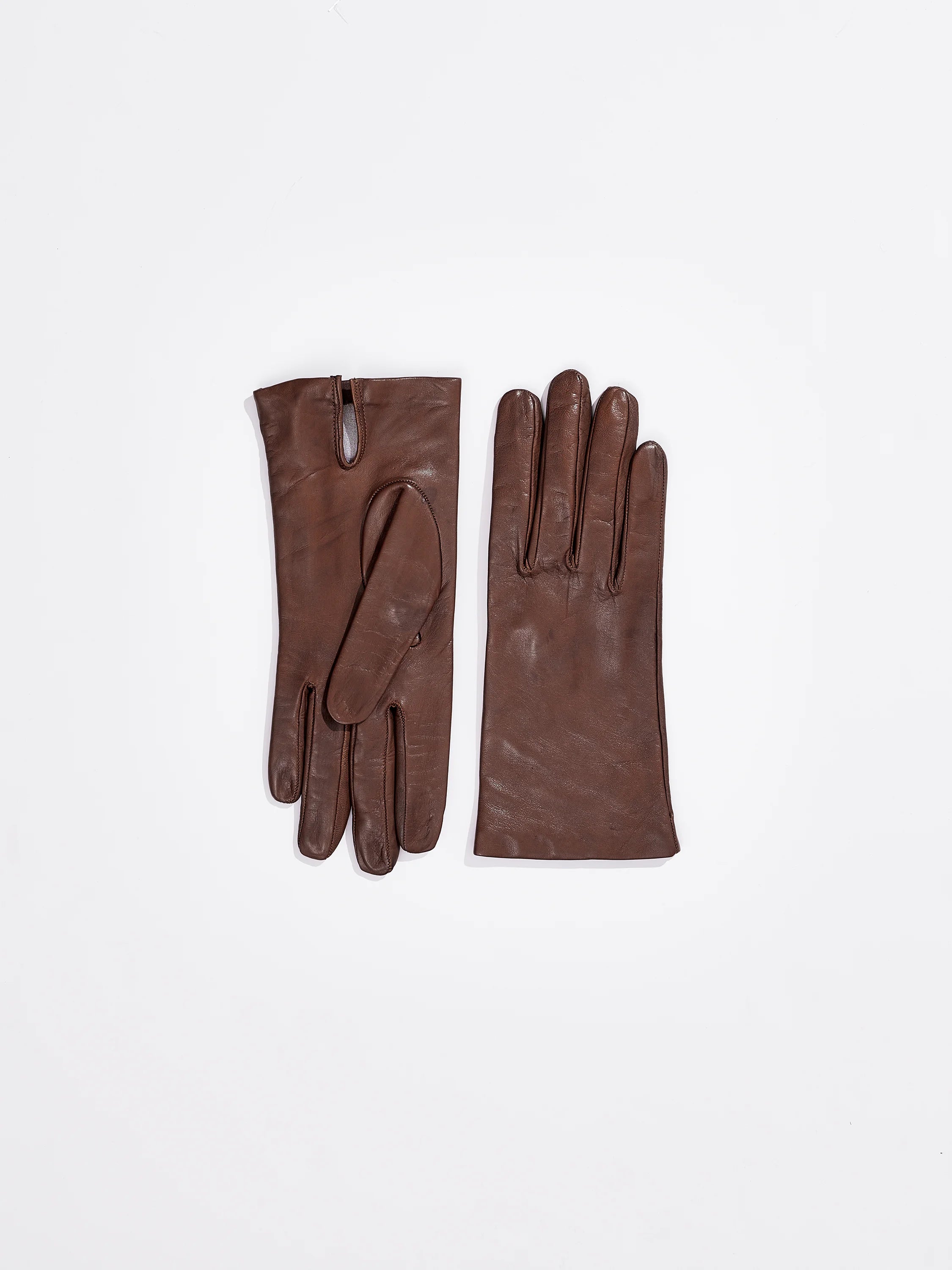 Pair of dark brown lambskin gloves. One glove folded, showing a wrist slit; the other laid flat.