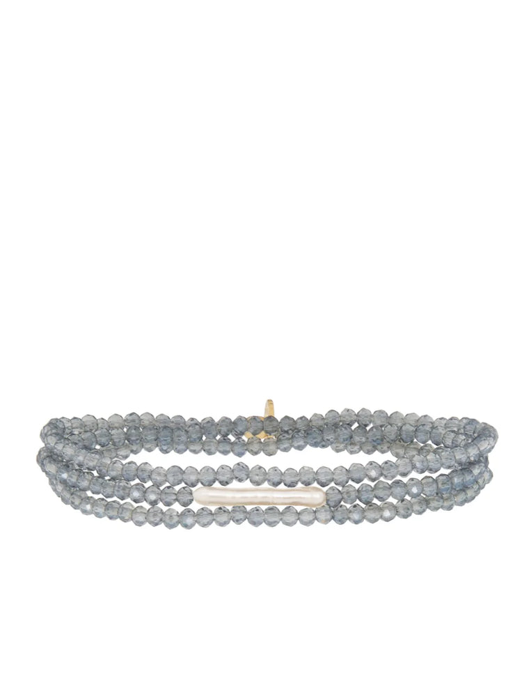 Multi-strand stretch bracelet: faceted blue-grey beads, horizontal off-white baroque pearl, small gold accent.