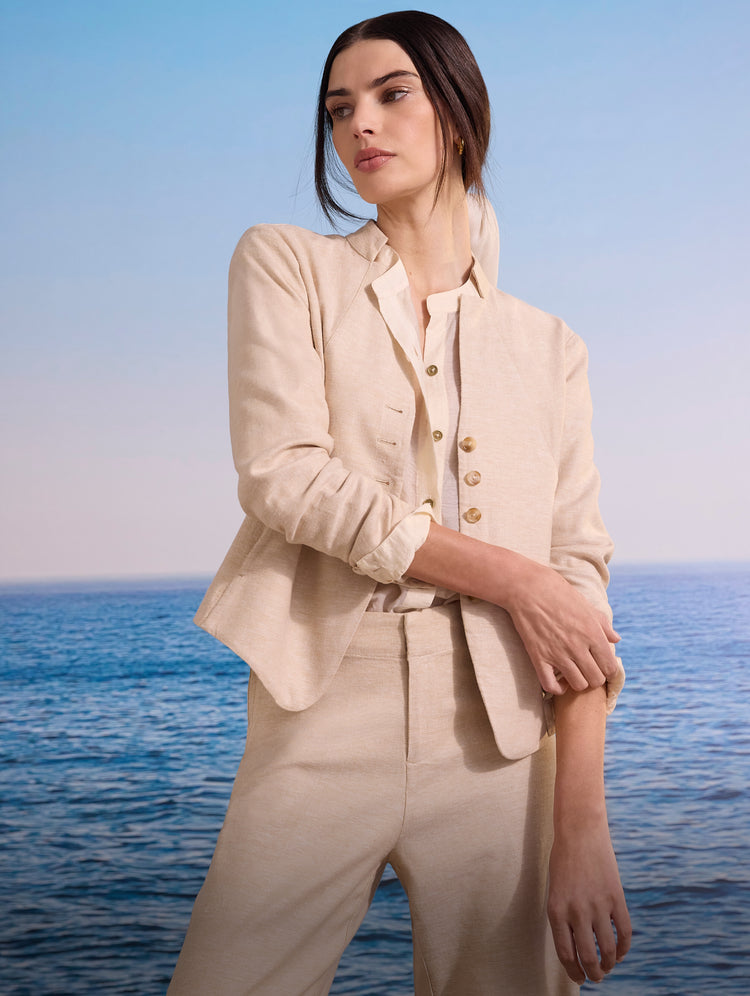 Woman wearing a light brown linen suit, with an ocean background.