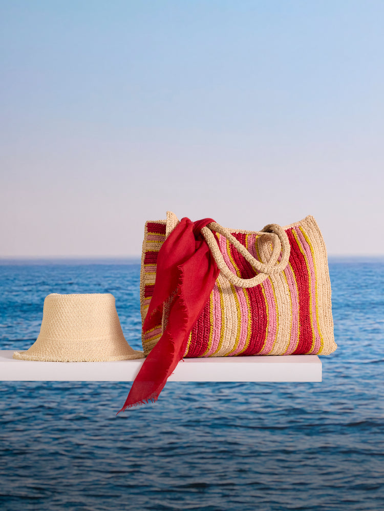 A straw tote bag and hat on a diving board over the ocean.