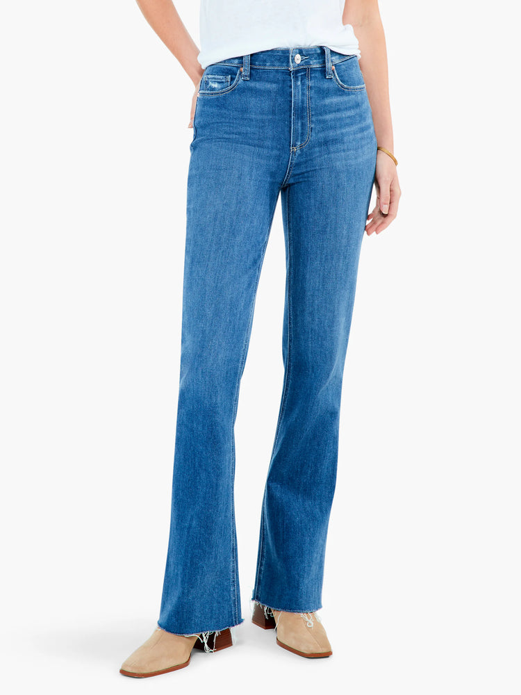 High-rise, medium-wash blue jeans with a flared leg and raw hem.  The model is wearing light beige shoes.