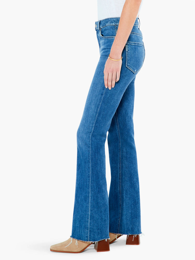 Blue, high-rise, flared jeans with a raw hem.  Shown on a model with tan shoes.