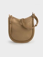 Beige leather hobo bag with a curved silhouette, adjustable strap, and small front pocket. Gold-toned hardware.