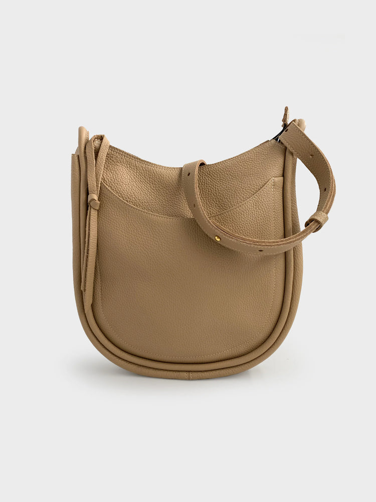 Beige leather hobo bag with a curved silhouette, adjustable strap, and small front pocket. Gold-toned hardware.