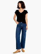 Dark wash blue, wide-leg ankle jeans with frayed hems; model wears a black v-neck top and tan shoes.