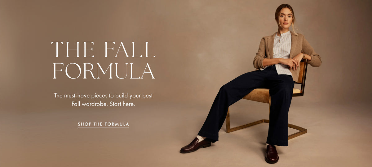 A woman sits on a modern chair against a warm beige studio background, wearing a tan blazer, white blouse, dark navy wide-leg trousers, and brown loafers. Large text on the left reads 'THE FALL FORMULA' with smaller supporting copy and a 'SHOP THE FORMULA' link.