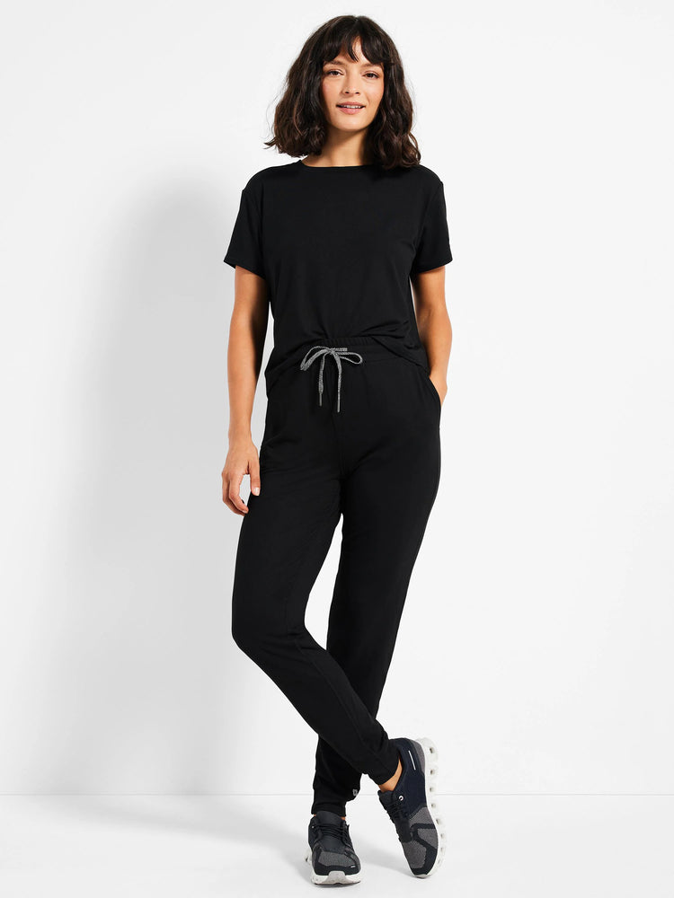 Black jogger pants with drawstring waist.  Features cuffed ankles.  Model is wearing them with a black short-sleeved top...