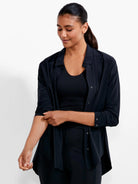 Black, collared, long-sleeve shirt with metallic snaps. Worn open, model rolls up sleeve.