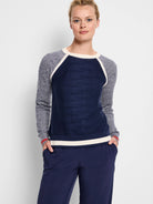 Navy blue sweater with grey/white speckled raglan sleeves and cream/navy stripes at hem and cuffs.  Red detail on cuffs.
