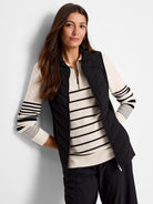 Black quilted puffer vest, zipper front.  Features diagonal quilting. Model wears it over an off-white horizontally...