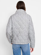 White quilted puffer jacket with grey irregular vertical stripe pattern. Features stand collar, back view.