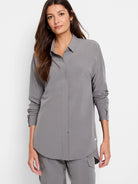 Grey collared long-sleeve shirt on a woman. Smooth fabric, loose fit, and sleeves pushed up.