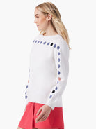 White sweater with a row of small, dark-blue, and black dots across the shoulders and down the sleeves.  Some dots are...