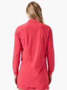 Back view of a woman wearing a coral red long-sleeve shirt with a collar and horizontal seam across the back.